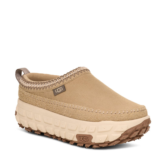 A mustard yellow UGG Venture Daze slipper with a suede upper, iconic box stitch, and a grippy outsole with tire treads.