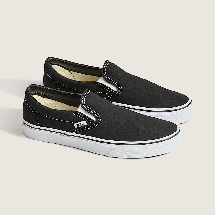 Pair of black slip-on sneakers with white soles on a light gray background